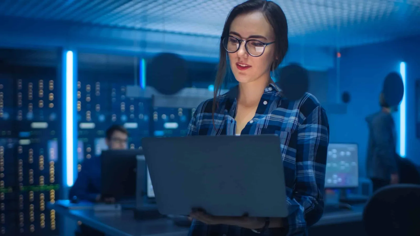 An engineer holding a laptop in a data center lit in blue
